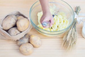 un cuisinier écrase des pommes de terre avec un presse purée pour faire une purée